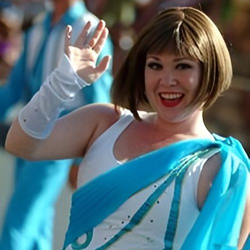 Woman in blue waving at event.