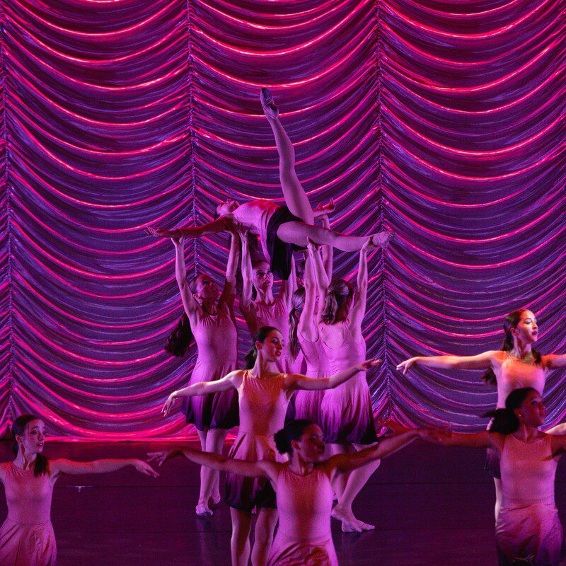 Dancers performing lift on pink-lit stage