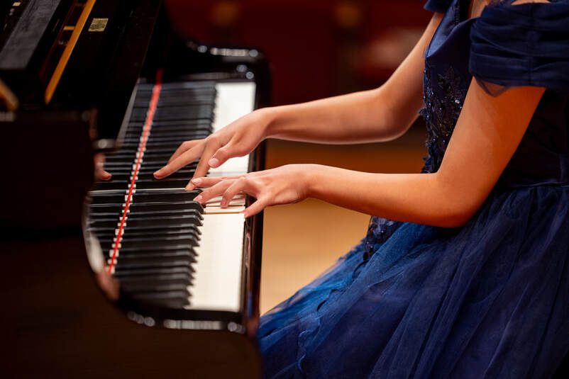 Pianist's hands on grand piano keys, blue dress